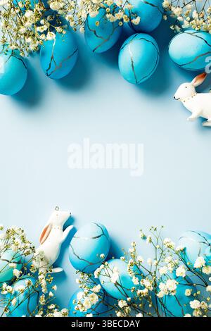 Blue Easter eggs with decorations and flowers on blue background. Vertical flat lay Stock Photo