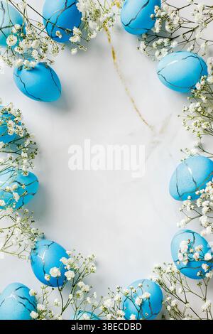 Frame of painted blue Easter eggs with flowers on marble table. Top view vertical Easter background Stock Photo