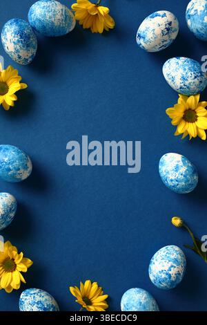 Easter vertical background, poster, banner design. Frame of blue and white painted Easter eggs with yellow flowers on dark blue background. Stock Photo