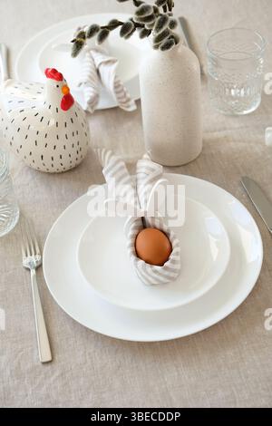 Easter table setting with Easter egg in rabbit napkin on plate and cutlery. Stock Photo