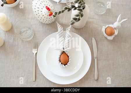 Easter setting table with Easter egg with rabbit ears made of napkin on plate. Stock Photo