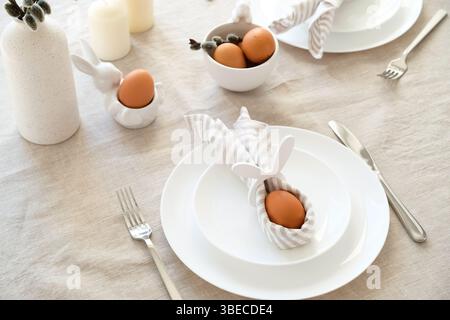 Rabbit Easter egg in napkin on plate. Easter dinner table setting concept. Stock Photo