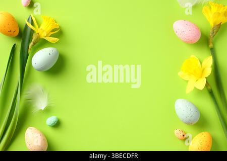 Happy Easter greeting card template. Frame made of colorful Easter eggs and yellow daffodil flowers on green table. Stock Photo