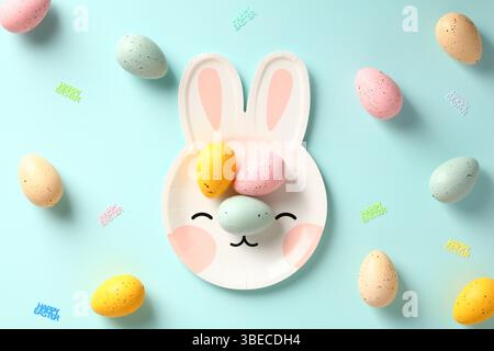Happy Easter flat lay composition. Cute Easter bunny plate and colorful eggs on blue background. Stock Photo