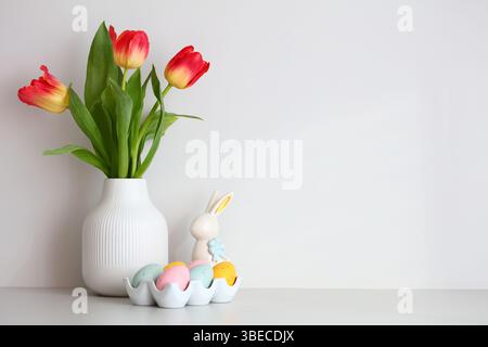 Vase of tulips, Easter bunny, Easter eggs on white wall background. Happy Easter concept. Stock Photo