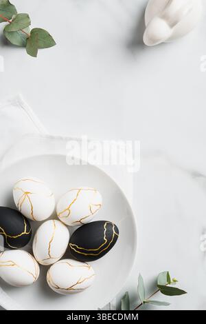 Happy Easter concept. Luxury Easter eggs, bunny rabbit, eucalyptus leaves on marble table. Flat lay, top view, vertical. Stock Photo