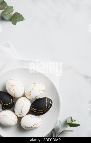 Luxury Easter eggs decorated with gold in plate and eucalyptus leaves on marble table. Flat lay, top view. Minimal style. Stock Photo