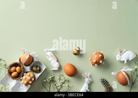 Easter flat lay composition with decorated eggs, ceramic bunnies, and flowers on a pastel green background Stock Photo