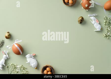 Easter flat lay with decorative eggs, ceramic bunnies, and flowers on a pastel green background Stock Photo