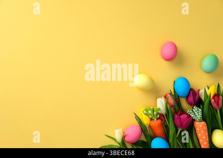 Colorful Easter eggs and spring tulips on a yellow background. Happy Easter greeting card template. Stock Photo