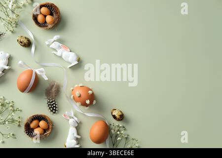 Happy Easter concept. Flat lay composition with decorated eggs, ceramic bunnies, bird nests, feathers, and white flowers on a light green background Stock Photo
