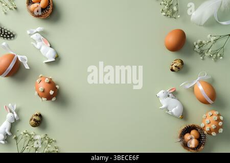 Happy Easter flat lay composition. Top view Easter eggs, quail eggs, gypsophila flowers, Easter bunny, feathers on pastel green background. Stock Photo