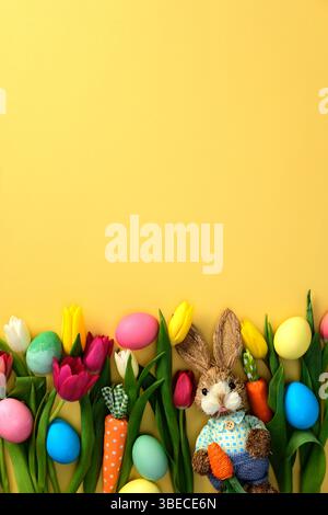 Flat lay composition with painted Easter eggs, tulips, bunny on yellow background Stock Photo