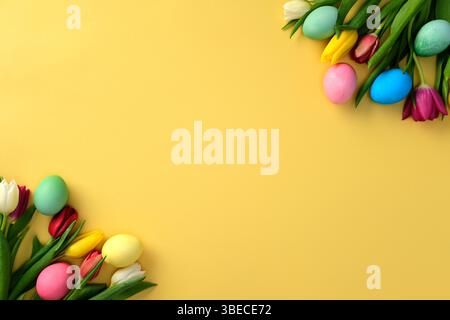 Colorful Easter eggs and vibrant tulips on a yellow background. Flat lay, top view, copy space Stock Photo