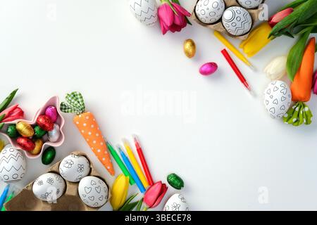 Easter flat lay with decorated eggs, tulips, chocolate eggs, and painting supplies on a white background. Stock Photo