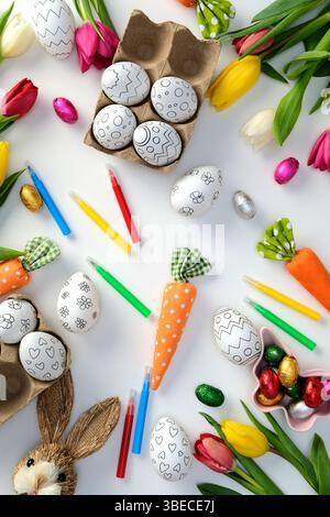 Happy Easter flat lay composition with Easter eggs for coloring, markers, tulips, Easter bunny on white background Stock Photo