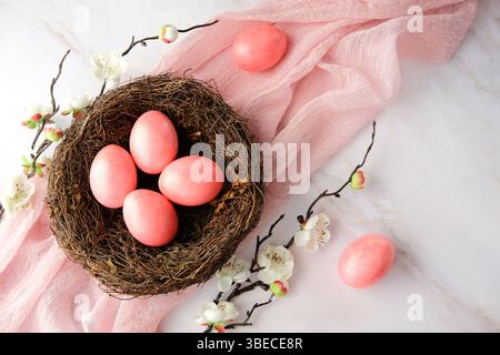 Pink Easter eggs in nest with blooming sakura branches on a soft pink fabric on marble background Stock Photo