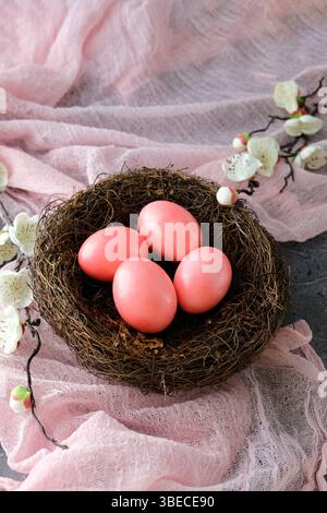 Nest with four pink Easter eggs, soft pink fabric background adorned with white flowers. Stock Photo