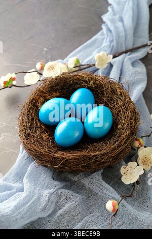 Blue Easter eggs in a nest with white cherry blossoms, set against a soft blue fabric Stock Photo