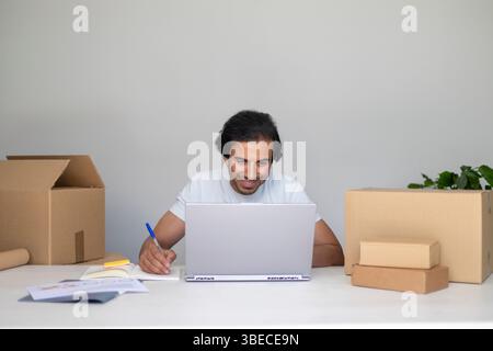 Smiling man multitasking with a laptop and notes, organizing his local business. Stock Photo