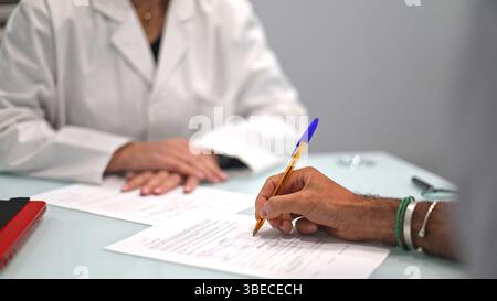 Close-up of doctor and patient filling out medical forms in a clinical office, focusing on hands and documents. Stock Photo