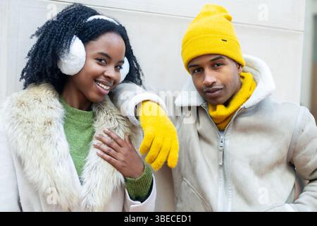 Young fashionable couple smiling and posing together in stylish winter clothes, radiating joy and warmth amidst the urban city backdrop Stock Photo