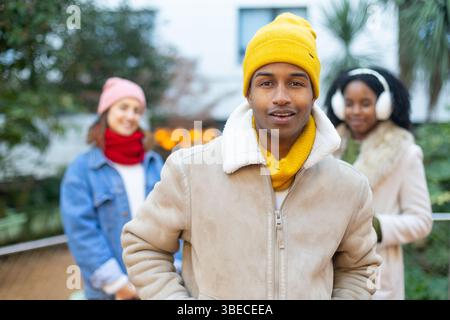 Portrait of a smiling young man wearing winter clothes standing outdoors with friends in the background Stock Photo