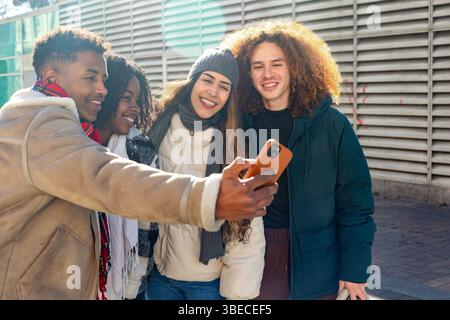 Four cheerful multi ethnic students taking a selfie outside their college on a sunny winter day Stock Photo