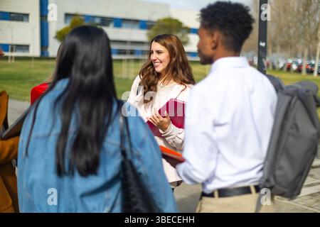 Group of diverse university students walking together on campus, holding notebooks and engaging in conversation Stock Photo