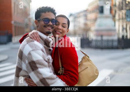 Happy multi ethnic couple embracing joyfully on a bustling city street, enjoying a romantic outing filled with love and connection Stock Photo
