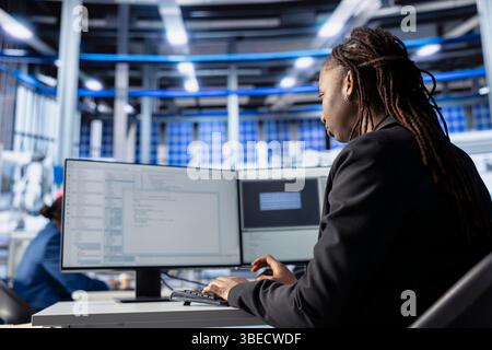 Engineer coding at workstation in solar panel manufacturing plant, developing programs to automate equipment processes. Photovoltaics factory expert writing scripts to optimize robotic operations Stock Photo