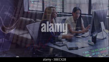 Statistical data processing against two diverse female office colleagues discussing at office Stock Photo