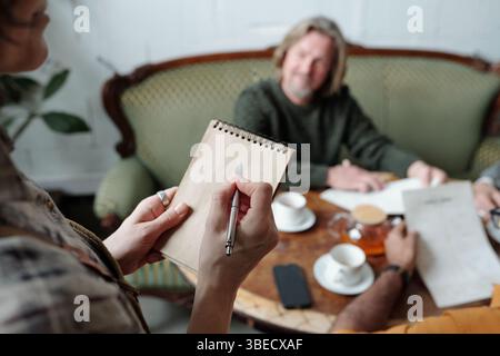 Group of colleagues engaging in collaborative discussion, with focus on one person writing notes while others interact Stock Photo