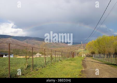 Fading rainbow over a rural landscape. Dirt road in the romanian countryside Stock Photo