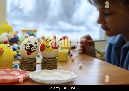 In the foreground there are decorated children's Easter eggs, in the background a child is painting an egg Stock Photo
