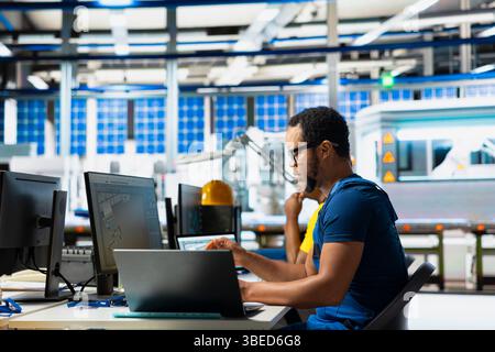 Black engineer testing solar technology at pc setup in renewable energy facility, focusing on software troubleshooting and performance metrics. Supports eco friendly sustainable operations. Stock Photo