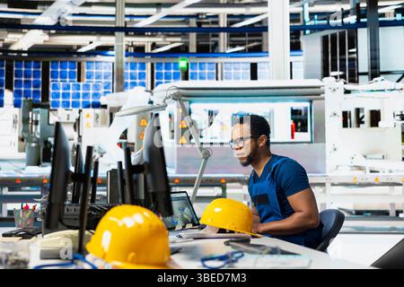 Male engineer using pc setup to oversee solar panel plant assembly lines, troubleshooting photovoltaic system to manage seamless production line with robotic arms. Renewable energy. Stock Photo