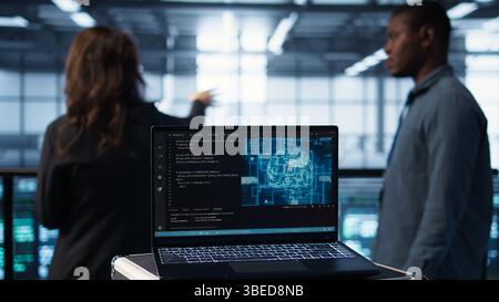Focus on laptop used by teamworking data center computer scientists in background using artificial intelligence. Notebook screen with neural networks doing computing processes, camera B close up Stock Photo