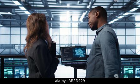 Software developers in data center using laptop, employing AI machine learning models. Workers using notebook to fulfill artificial intelligence infrastructure needs, allocating resources, camera B Stock Photo
