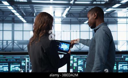 Data center technicians deploying AI driven management tools using tablet. Server farm coworkers inspecting server clusters, updating network topologies using artificial intelligence, camera B Stock Photo