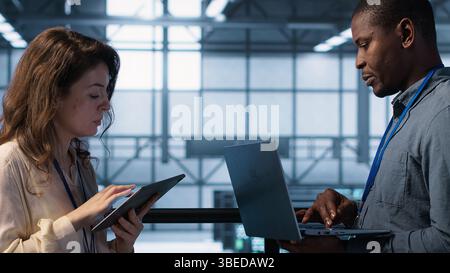 Team of technicians working in server farm, using laptops to analyze data. Teamworking workers examining infrastructure in data center, ensuring system integrity and security, camera A Stock Photo