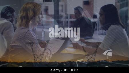 Statistical data processing against two diverse female office colleagues discussing at office Stock Photo