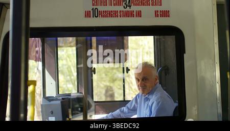 Steering senior driver focusing on road ahead through front window at bus cabin, with fare machine Stock Photo