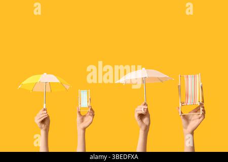Female hands holding mini deck chairs with umbrellas on yellow background Stock Photo