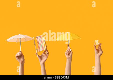 Female hands holding mini deck chairs with umbrellas on yellow background Stock Photo