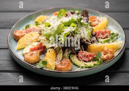 Delicious shrimp salad with grilled prawns, orange slices, avocado, greens, and parmesan cheese served on a plate in a restaurant setting Stock Photo