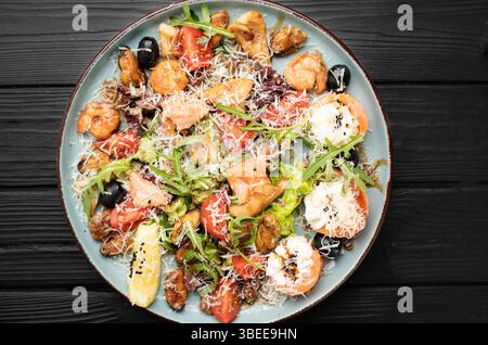 Delicious seafood salad featuring grilled shrimp, mussels, salmon, cream cheese, Parmesan, arugula, and lemon slices, artfully arranged on a large pla Stock Photo