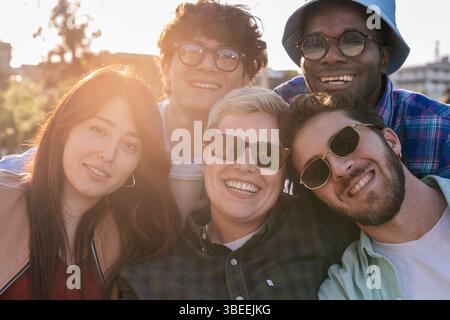 Diverse group of young friends enjoying time together outdoors at sunset, smiling and embracing authentic friendship and happiness Stock Photo