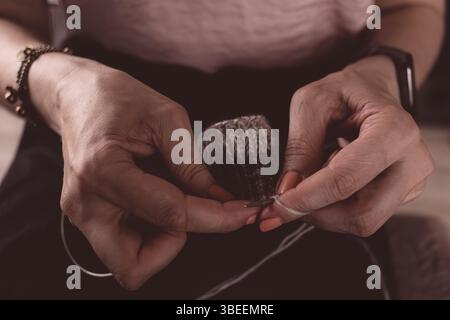 Knitting needles in a woman s hand. Knitted items. Self-made warm socks. Knitting pattern. Quality wool thread. Winter clothes. Christmas gift. Stock Photo