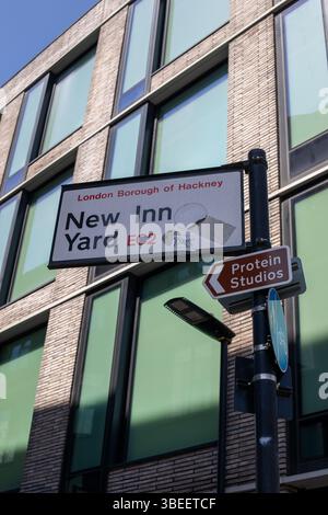 Street signs, including New Inn Yard, in front of a modern building in Hackney, London. The signs point towards Protein Studios. Stock Photo